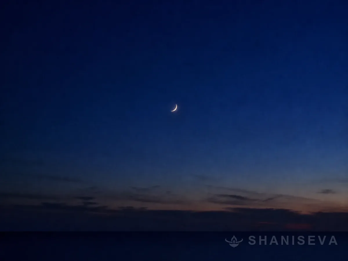 A thin crescent moon in a deep indigo sky
